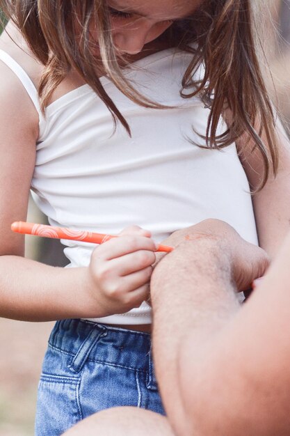 Tochter schreibt auf die Hand des Vaters mit einem orangefarbenen Filzstift