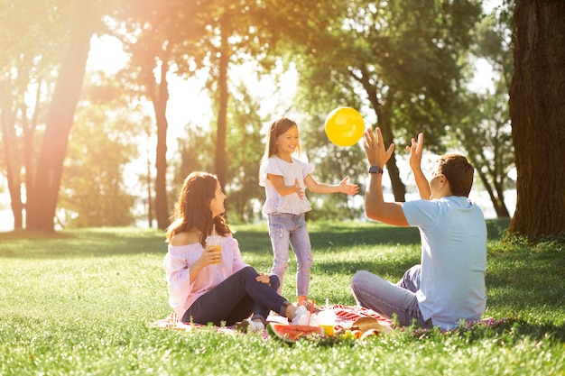 Tochter spielt Ballon mit Eltern im Park an einem sonnigen Tag