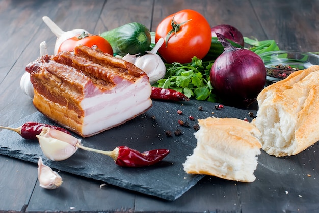 Tocino ahumado con baguette y verduras en tablero de piedra negro