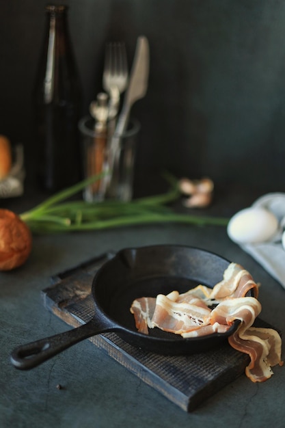 Tocino en una sartén de hierro fundido sobre la mesa en casa Cocinar huevos revueltos con tocino