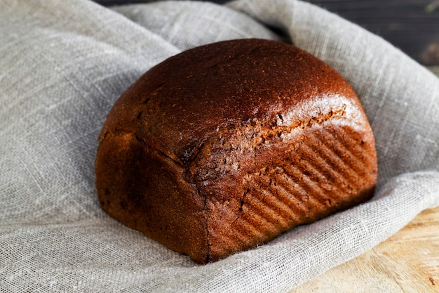 Toda una hogaza de pan negro sobre una tabla de cortar, un primer plano de pasteles caseros sobre un mantel