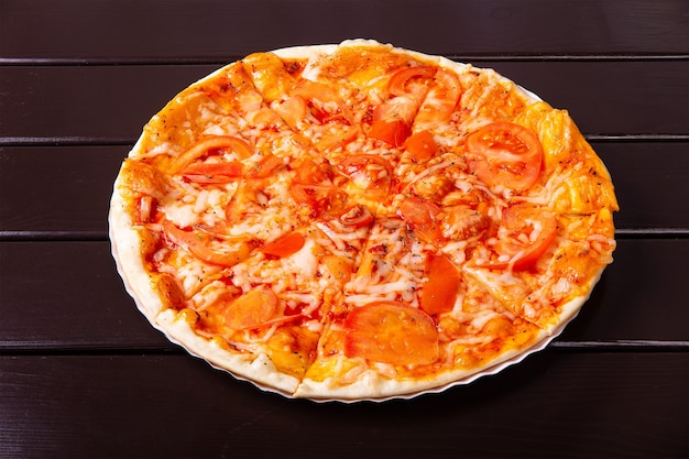 Toda una pizza rústica Margarita con mozzarella, tomate y albahaca se sirve en un plato de papel sobre una mesa de madera