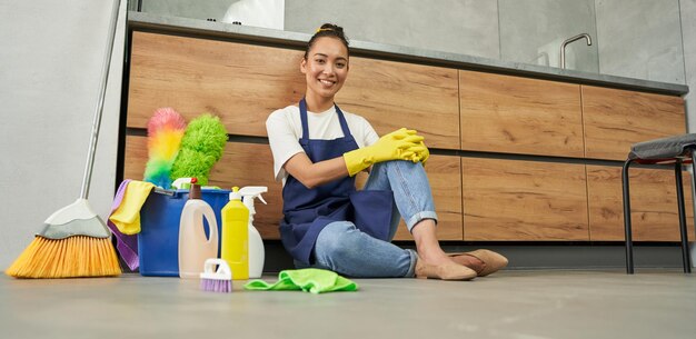 Todas las superficies limpian a una hermosa joven sonriendo a la cámara mientras descansa después de limpiar el piso con