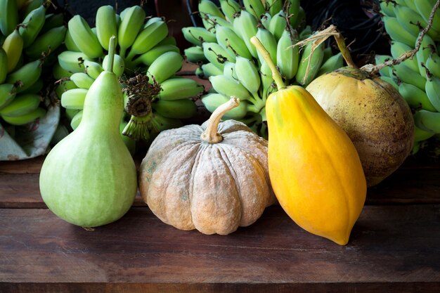 Todavía vida con la calabaza, la papaya, el coco, la calabaza y el plátano en vintage de madera.