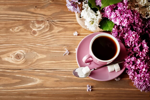 Todavía vida con las ramas de la lila y una taza de café en una tabla de madera.