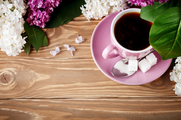 Todavía vida con las ramas de la lila y una taza de café en una tabla de madera.