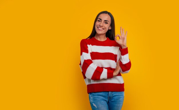 ¡Todo bien! Sonriente linda joven morena muestra un signo de ok en la cámara en el estudio