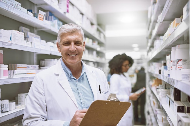 Todo en un día de trabajo como farmacéutico Retrato de un alegre farmacéutico masculino maduro sosteniendo un portapapeles y haciendo acciones mientras mira la cámara en una farmacia