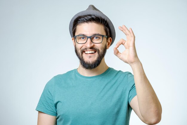 Todo está bien joven feliz haciendo gestos de OK y sonriendo contra un fondo gris