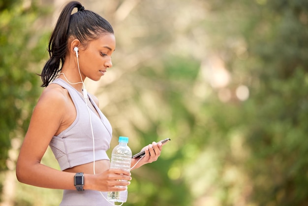 Todo el mundo tiene esa canción para sentirse bien. Una foto de una joven deportista que usa un celular mientras hace ejercicio al aire libre.