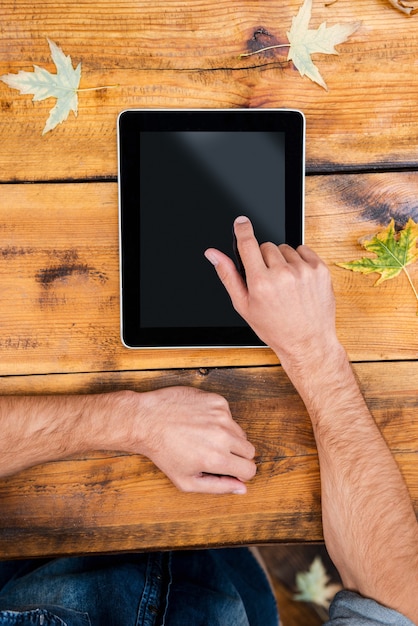 Foto todo o mundo em um toque. close de um homem segurando o dedo em um tablet digital enquanto está sentado à mesa de madeira ao ar livre