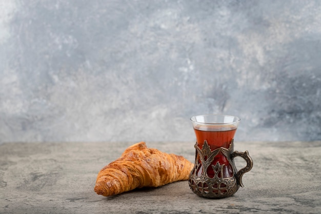 Todo un sabroso croissant de mantequilla con una taza de té colocada sobre una mesa de piedra.