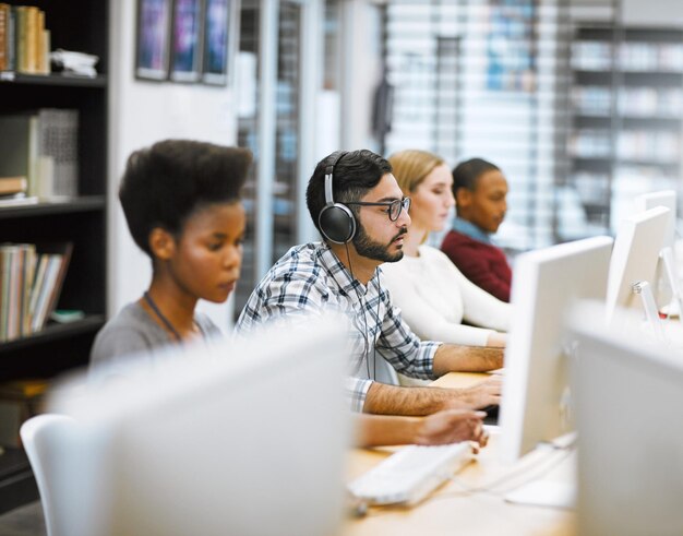 Todos vamos a estar aquí por un tiempo Foto de un grupo de estudiantes enfocados trabajando en computadoras investigando para los exámenes dentro de una biblioteca