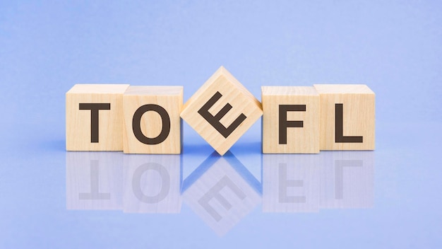 TOEFL-Wort steht auf Holzwürfeln auf blauem Hintergrund, Nahaufnahme von Holzelementen