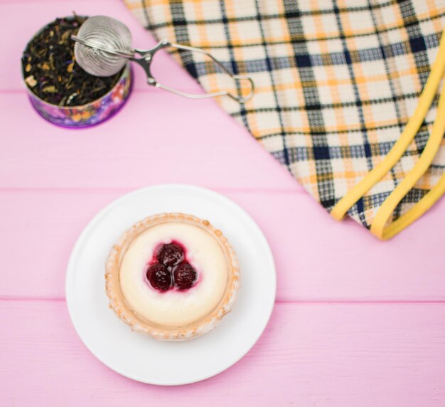 Törtchen mit Beeren und Sahne auf einem weißen Teller auf einem rosafarbenen Holzhintergrund