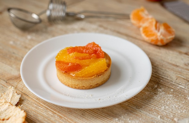 Törtchen mit Mandarine und Grapefruit liegt auf einem Teller auf einem schönen Dessert aus Holztisch