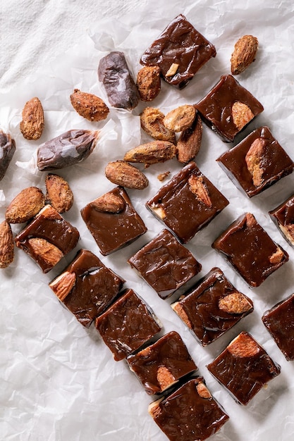 Toffee caseiro caramelo salgado chocolate amêndoas doces em papel amassado em linha sobre toalha de mesa de linho branco. presentes doces de comida artesanal para todos os feriados. postura plana