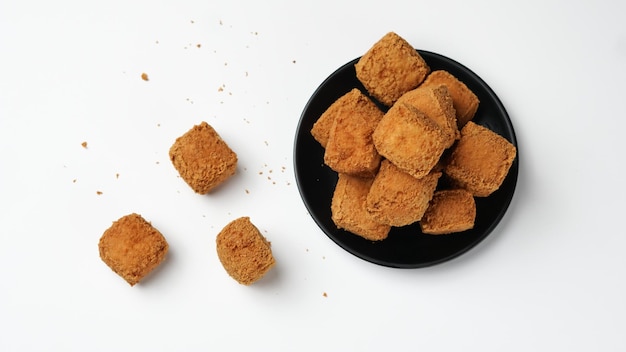 Tofu frito sobre un plato negro sobre fondo blanco.