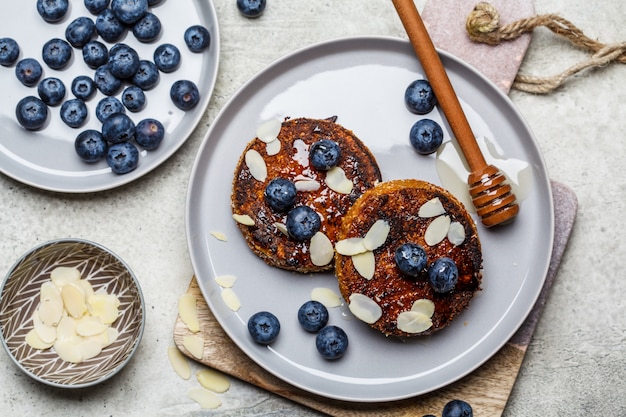 Tofu-Pfannkuchen mit Blaubeeren und Honig auf grauem Teller, Draufsicht. Gesundes veganes Lebensmittelkonzept.