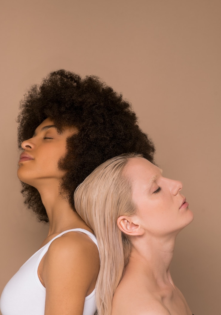 Foto togerherness. uma mulher de cabelos escuros e uma loira em pé, costas contra costas