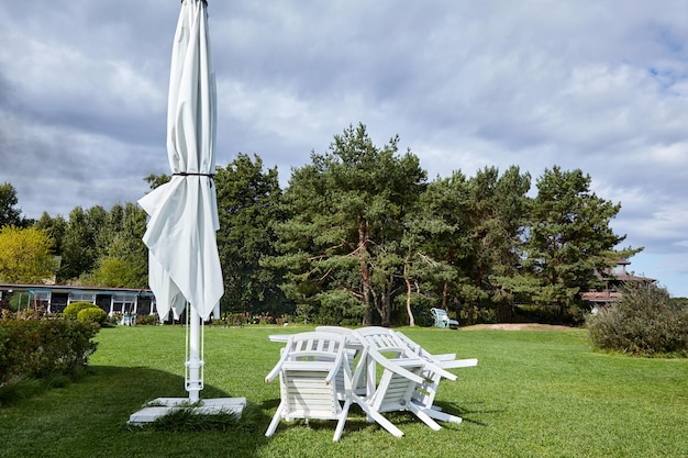 Toldo de guarda-chuva coberto para piquenique e cadeiras de madeira montadas e mesa no gramado verde de verão O café de verão no final da temporada está fechado