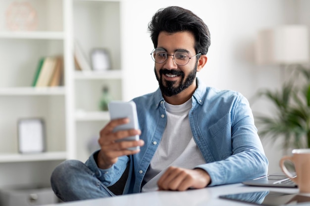 Tolle App lächelnder indischer Mann mit Smartphone im Heimbüro