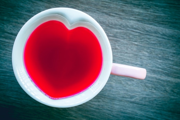 Tom de cor suave vintage com néctar vermelho de coração de vidro na xícara de fundo de madeira do amor dia dos namorados