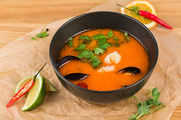 Tom ñame sopa con camarones y mejillones en un recipiente sobre una superficie de madera clara de cerca.