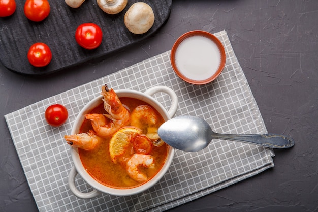 Tom ñame sopa con camarones en un plato sobre la mesa sobre una servilleta junto a champiñones y tomates. Foto horizontal