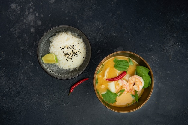 Tom Yam sopa servida con arroz vista superior sobre fondo rústico negro