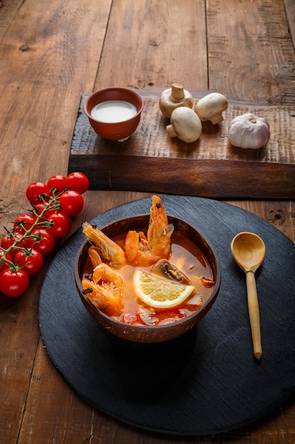 Tom Yamsuppe mit Garnelen und Kokosmilch auf dem Tisch auf einem runden Brett in der Nähe von Milchpilzen und Tomaten.