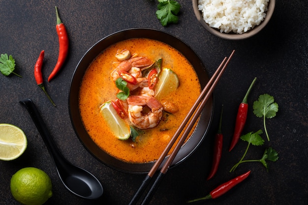 Tom Yum Kung Sopa tailandesa picante con camarones en un recipiente negro sobre una superficie oscura, vista superior