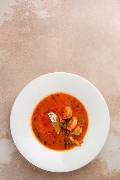 Tom yum en plato blanco sobre fondo de hormigón. Comida tailandesa picante con ingredientes en la mesa. Vista superior de la comida tailandesa picante