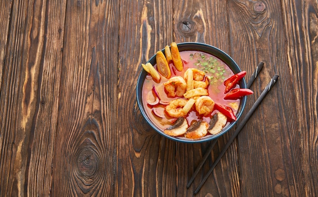 Tom Yum sopa picante con camarones, mariscos, leche de coco y ají en un tazón de cocina de comida tradicional asiática sobre fondo de madera