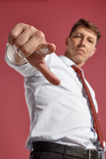 Toma de abajo hacia arriba de una persona morena guapa con ojos marrones, vestida con una camisa blanca y una corbata de terracota. Está jugando mientras posa en un estudio con un fondo rojo. Concepto de gestual