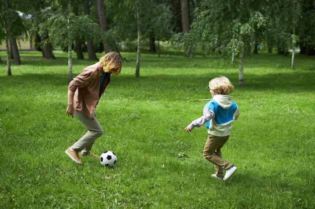 Toma de acción de padre e hijo jugando al fútbol juntos sobre la hierba verde en el parque