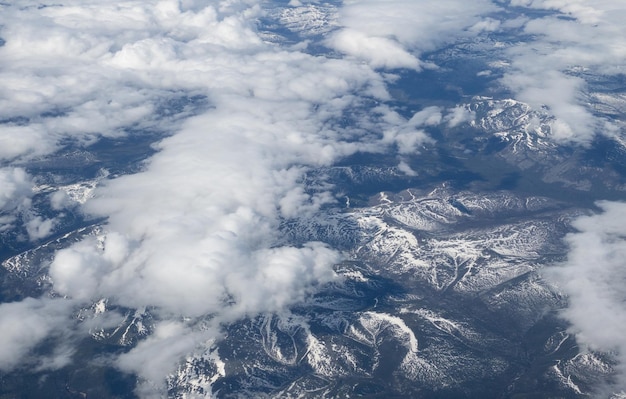 Toma aérea de cimas de montañas boscosas nevadas con nubes estratosféricas