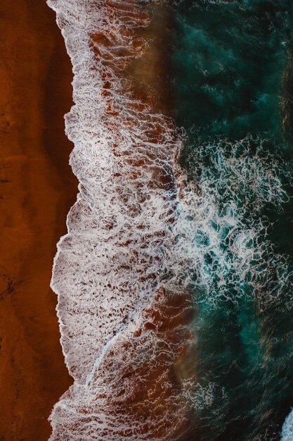 Toma aérea de las olas del mar rodeadas por una playa perfecta para fondos de pantalla y fondos