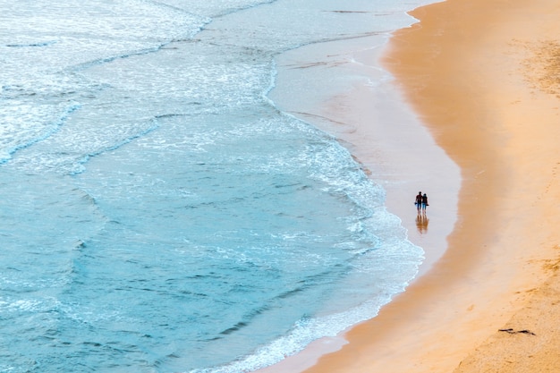 Toma aérea de una pareja en un mar ondulado y una playa de arena