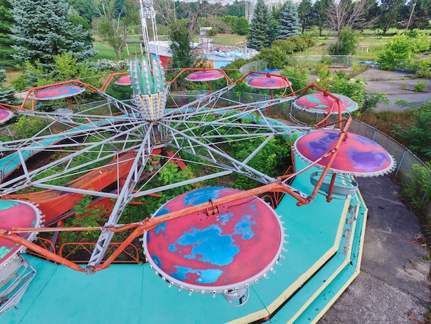 Foto toma aérea de un tilt a whirl en un parque temático abandonado rodeado de árboles y pastos