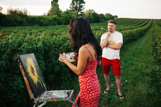 Toma al aire libre de una joven artista pinta un cuadro al aire libre Lección de pintura en la naturaleza Atractiva rubia viste casualmente pinta paisajes en un prado de primavera Pincel sobre lienzo creando y concepto de arte