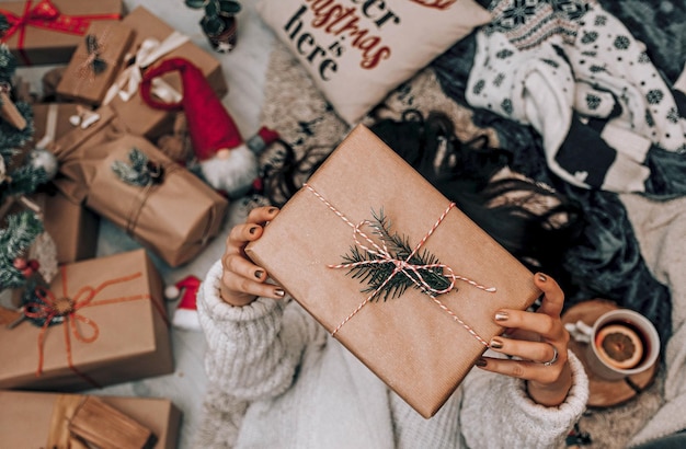 Toma en ángulo alto de una mujer sosteniendo una caja de regalo marrón acostada en la alfombra
