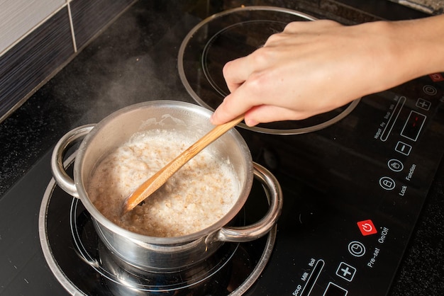 Toma en ángulo alto de una persona que cocina avena con leche en una olla en la estufa