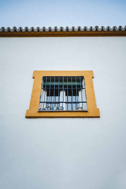 Toma en ángulo bajo de una ventana amarilla enmarcada en una pared blanca en España