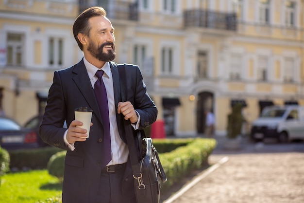 Toma un café. Alegre empresario sonriente de pie al aire libre mientras va a trabajar