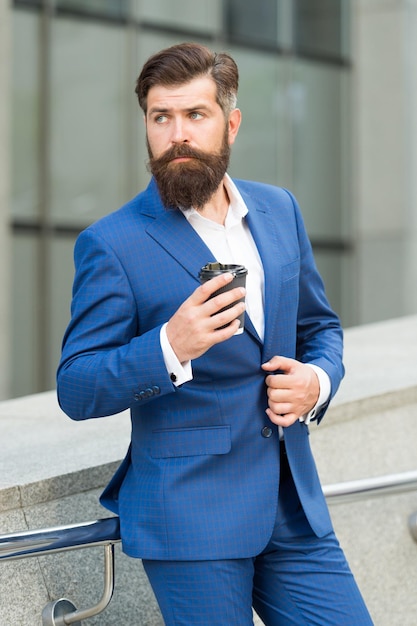 Toma un café serio Hombre profesional sostiene una taza al aire libre Hombre barbudo usa traje de negocios Descanso para tomar café Estilo de moda formal Trabajo y ocupación Empleado de oficina Construcción de carrera