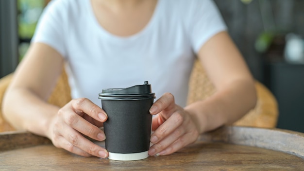 Toma cerca de una mujer sosteniendo una taza de café para llevar colocada sobre la mesa.