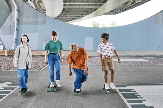 Toma completa de un grupo diverso de adolescentes montando patinetas en el espacio de copia del área de patinaje urbano