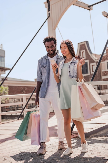 Toma completa de un hombre y una mujer jóvenes usando un teléfono inteligente después de ir de compras caminando por la calle