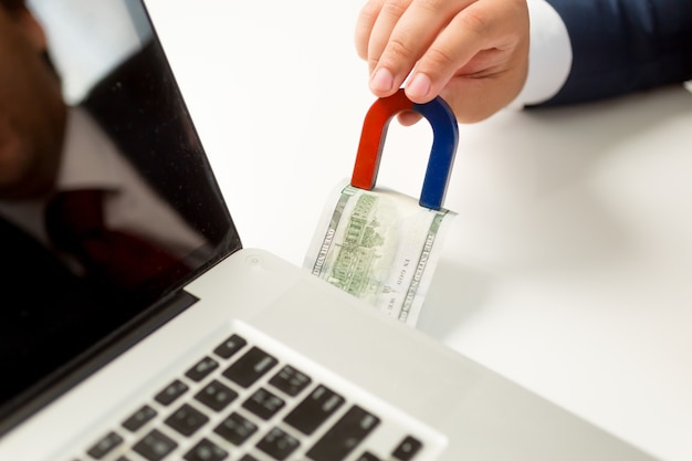 Toma conceptual de robar dinero en internet. Hombre tirando dinero de la computadora con imán